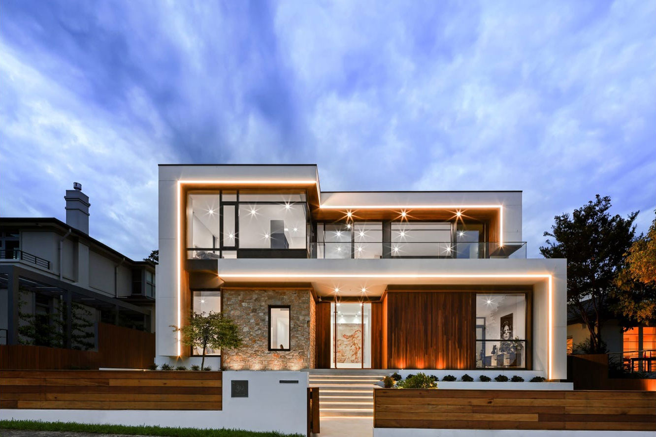 Facade of an ultra modern home lit up from below, with blue skies