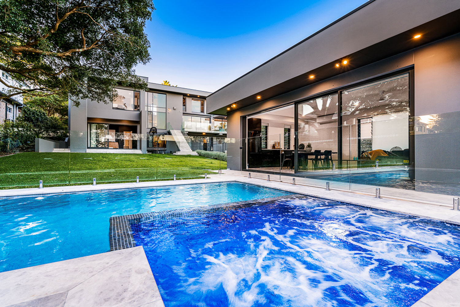 Low angle up of a blue pool and spa and an ultra-modern home