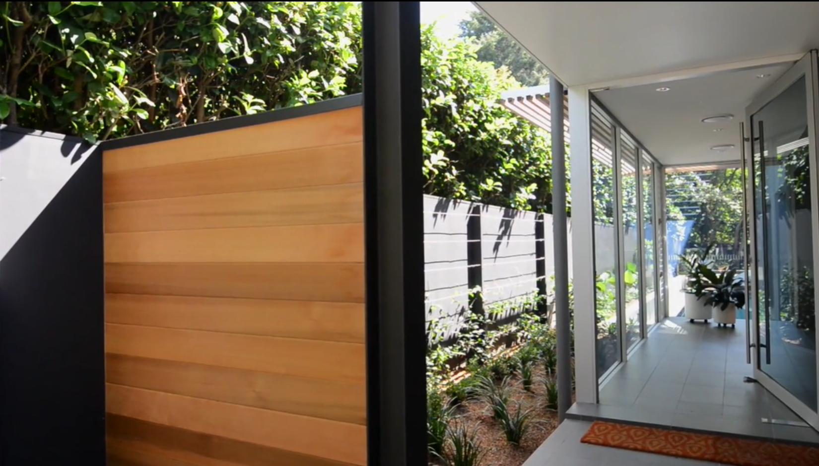 Entrance to a modern home, with wooden slats, charcoal metal beams and floor to ceiling glass