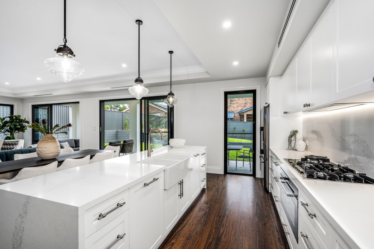 White kitchen with large stone island bench, pendant lights, gas cooktop and connection to the dining area