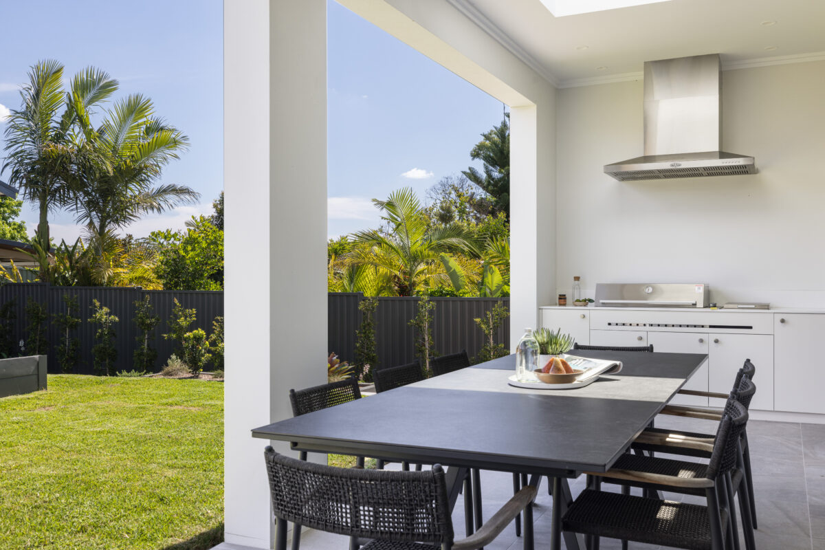 Covered alfresco dining area with built-in barbecue, outdoor table and views across the landscaped backyard