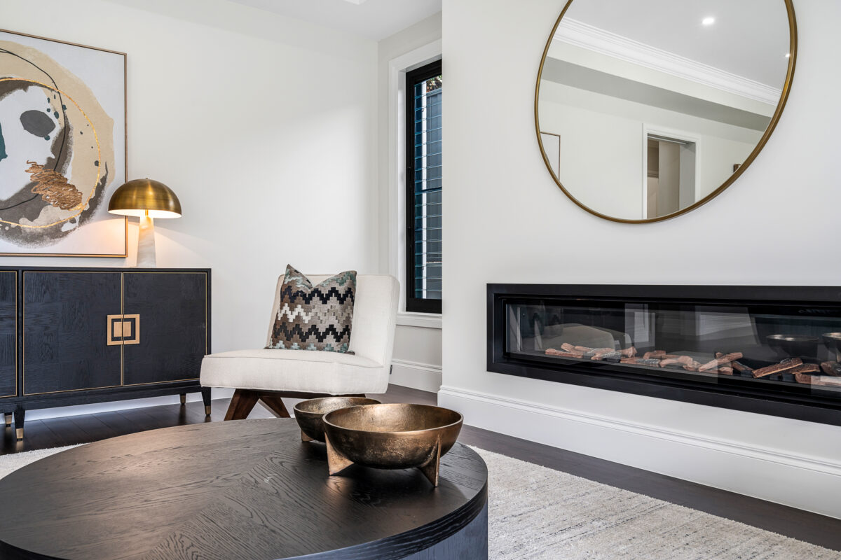 Luxury living room with feature fireplace, round mirror, armchair, artwork and dark timber flooring