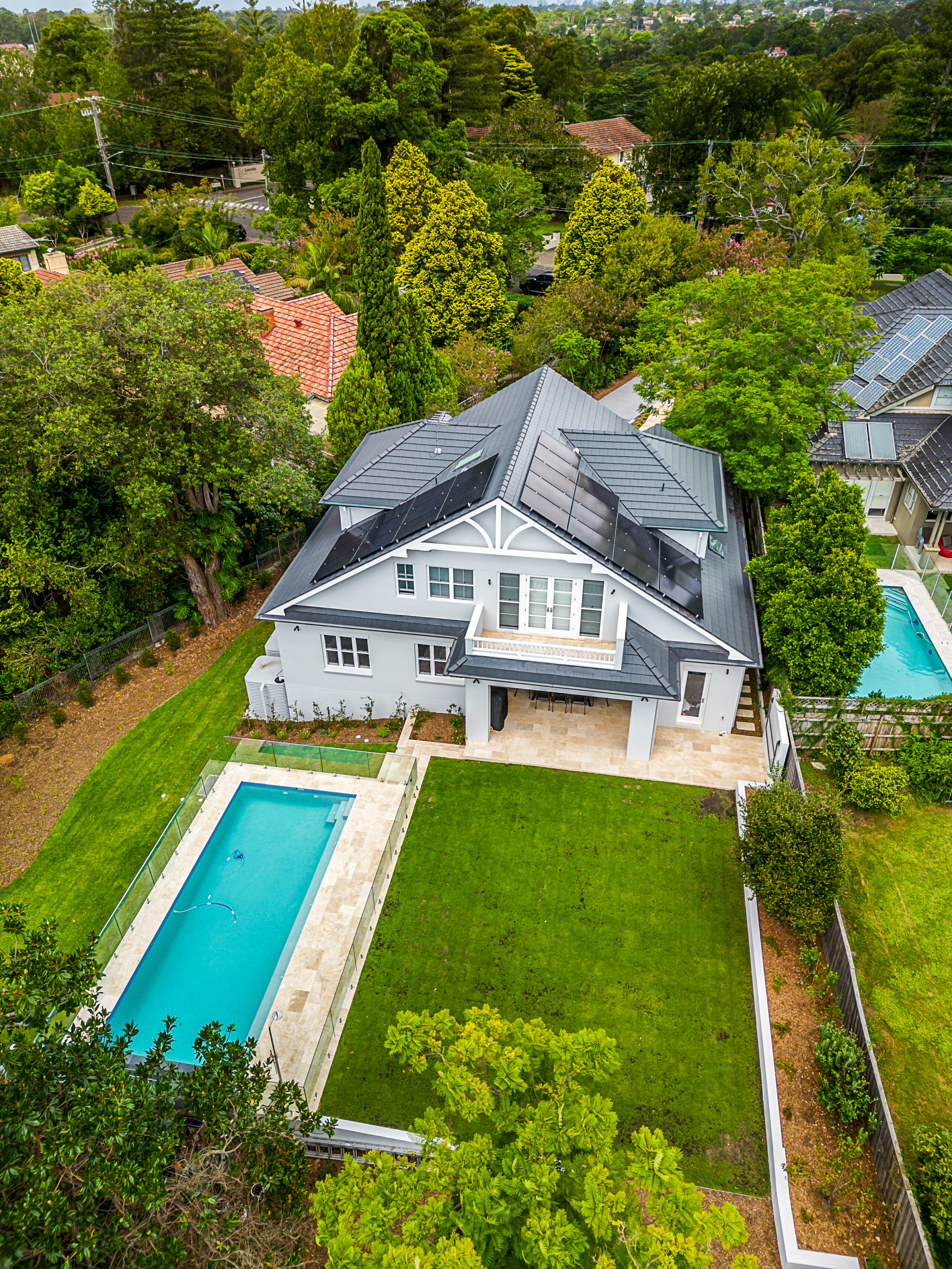 Aerial view of a Contemporary Hamptons custom home with a swimming pool, lawn and landscaped gardens.