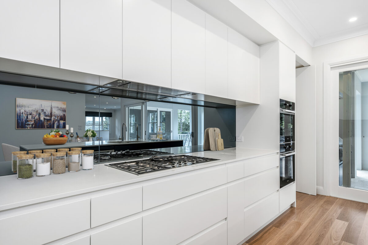 Contemporary white kitchen with a gas cooktop, mirrored splashback and streamlined joinery