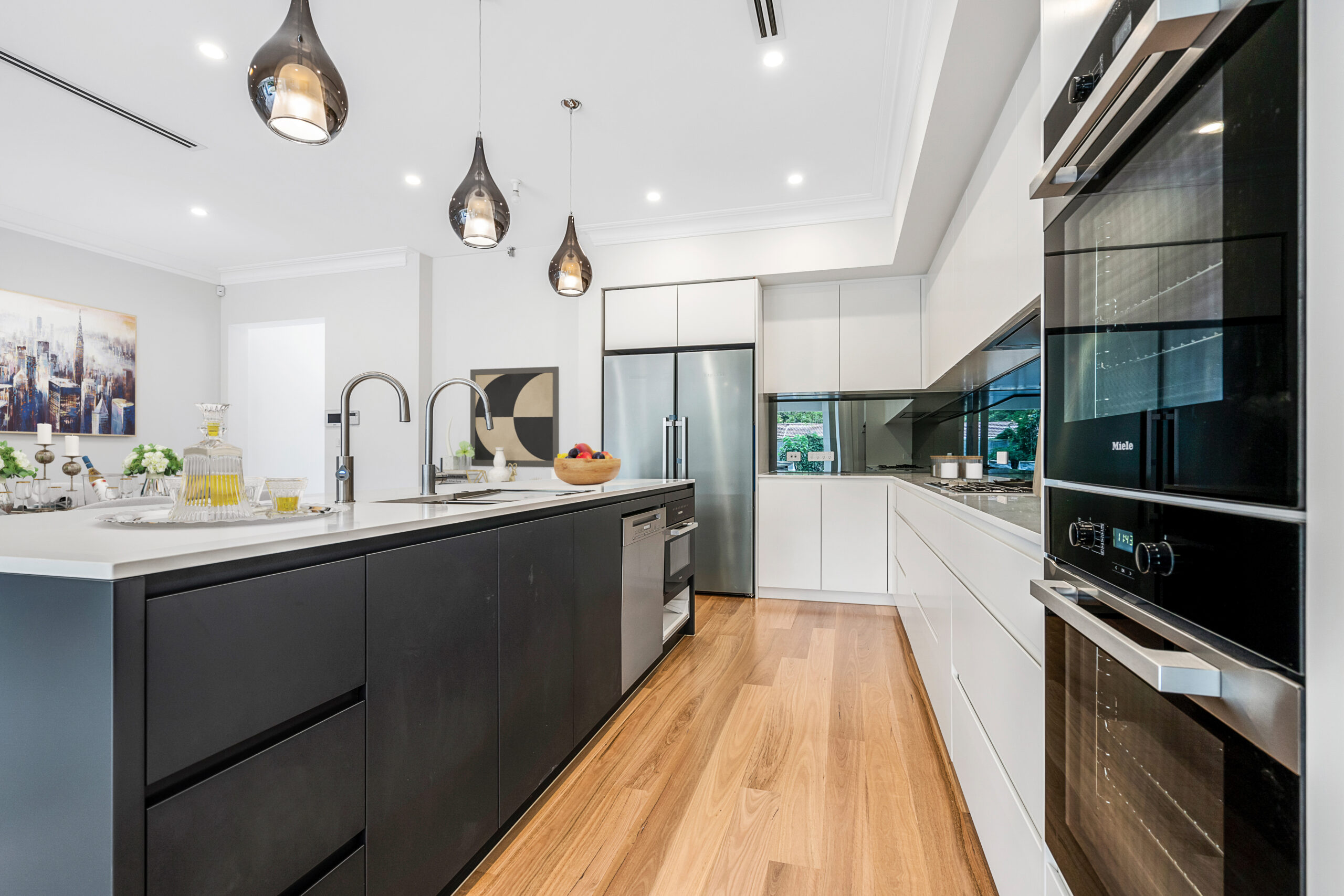 Premium black and white kitchen with an island bench, pendant lighting and integrated appliances.