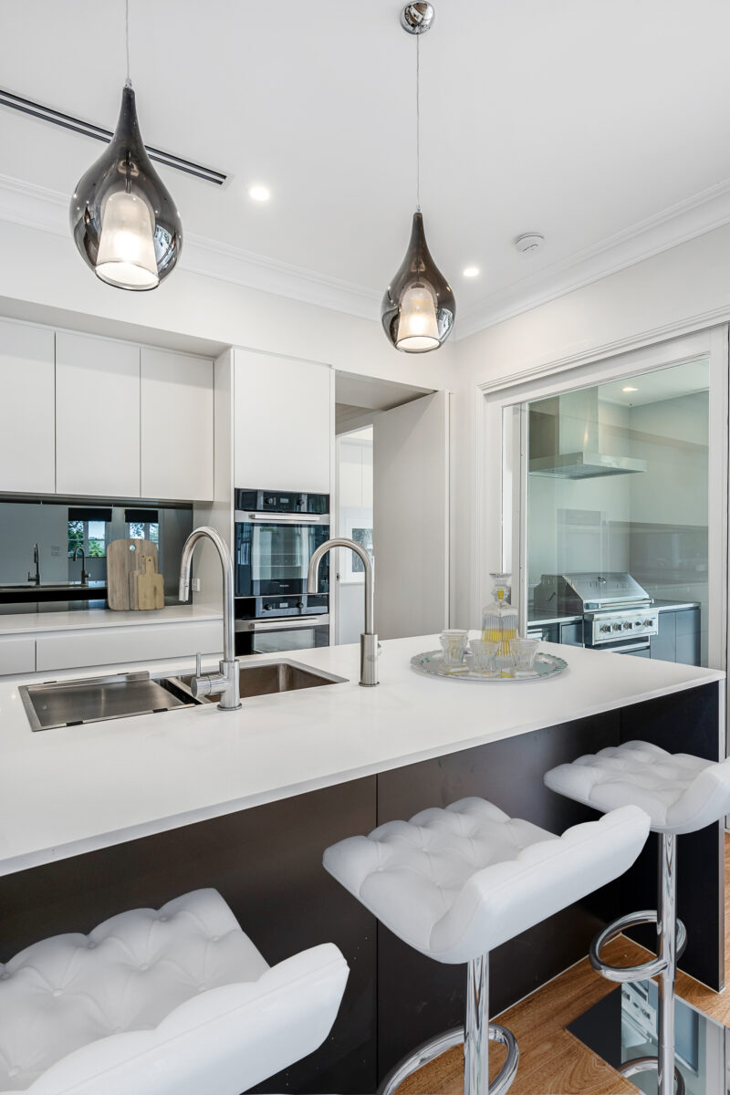 Kitchen island with a waterfall benchtop, sculptural pendant lights and upholstered bar stools.