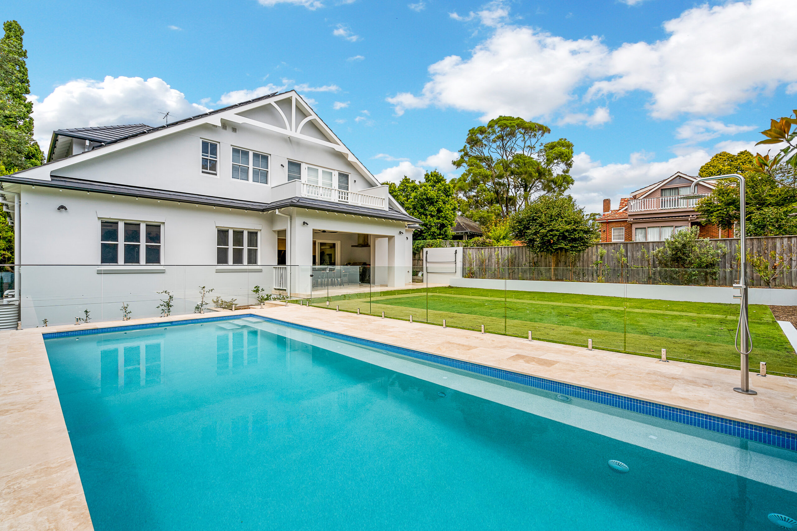 Rear view of one of Chateau’s Contemporary Hamptons custom homes with a pool, lawn and covered alfresco area